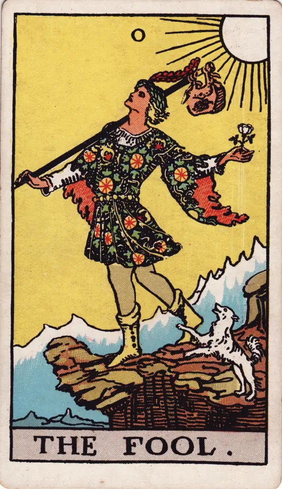 The Fool from the 1909 deck: a young traveller in a bright tunic steps toward a cliff edge under a yellow sky, a white rose in one hand, a small dog at his heels.